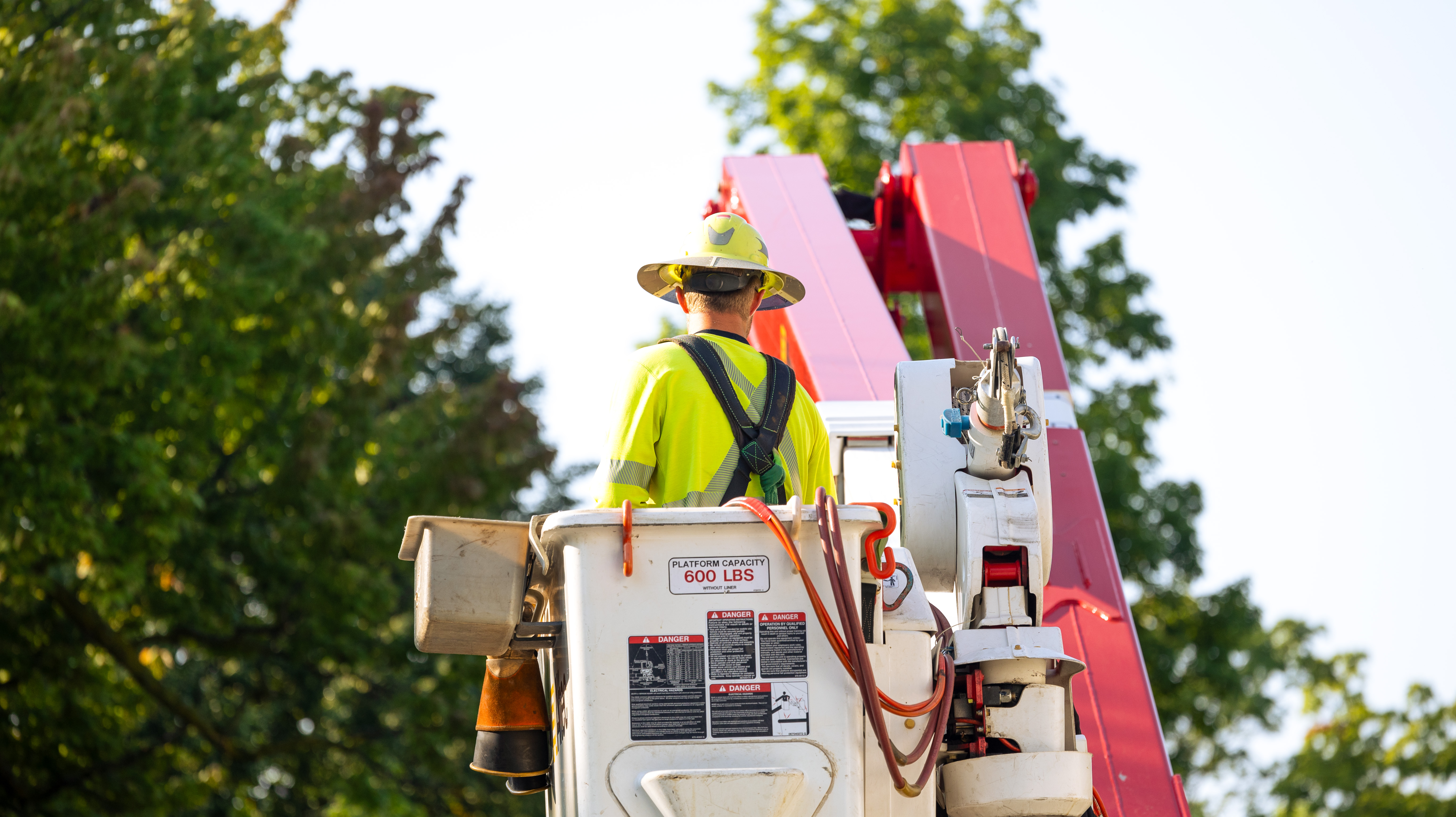 A lineworker in a hat stands in the bucket of a bucket truck.